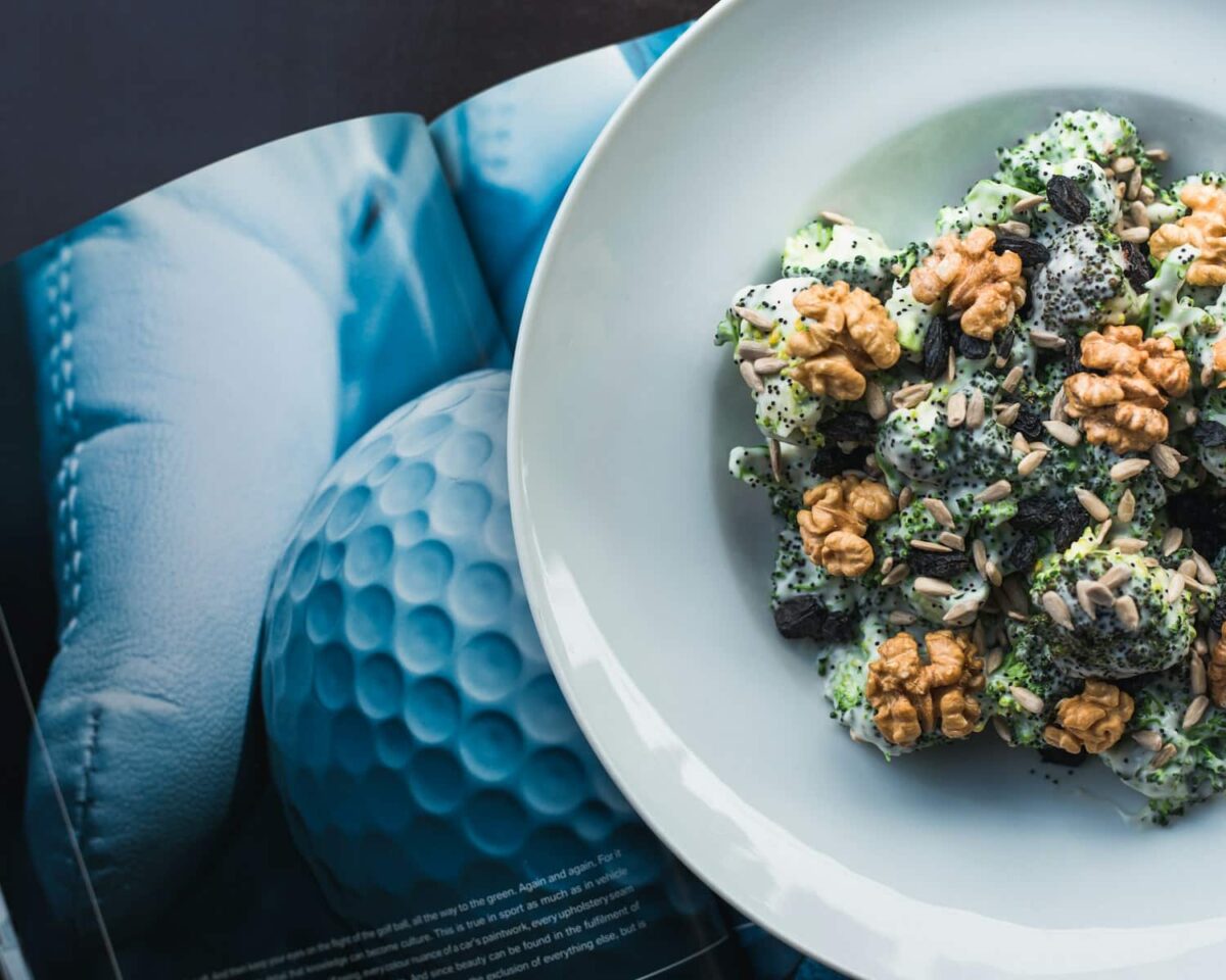 cooked dish on round white ceramic plate on top of open book, Broccoli Salad