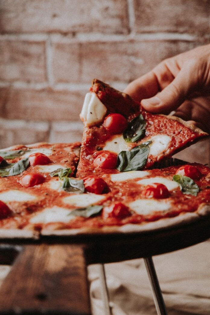 person holding sliced pizza with red sauce, Cauliflower Pizza Crust