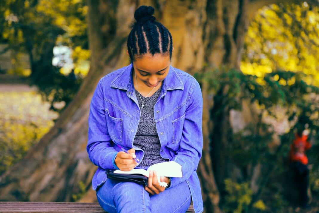 selective focus photography of woman reading book while sitting at bench