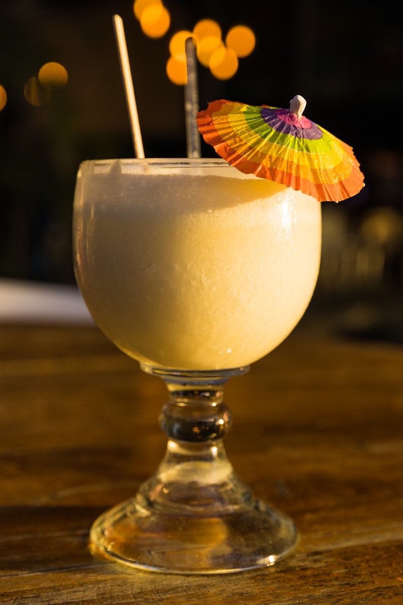 clear drinking glass with yellow liquid and purple and yellow flower, Piña Coladas