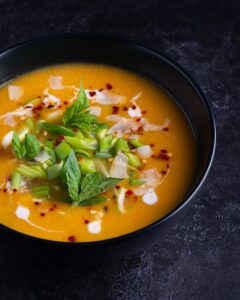 thai pumpkin soup soup with green leaf on black ceramic bowl