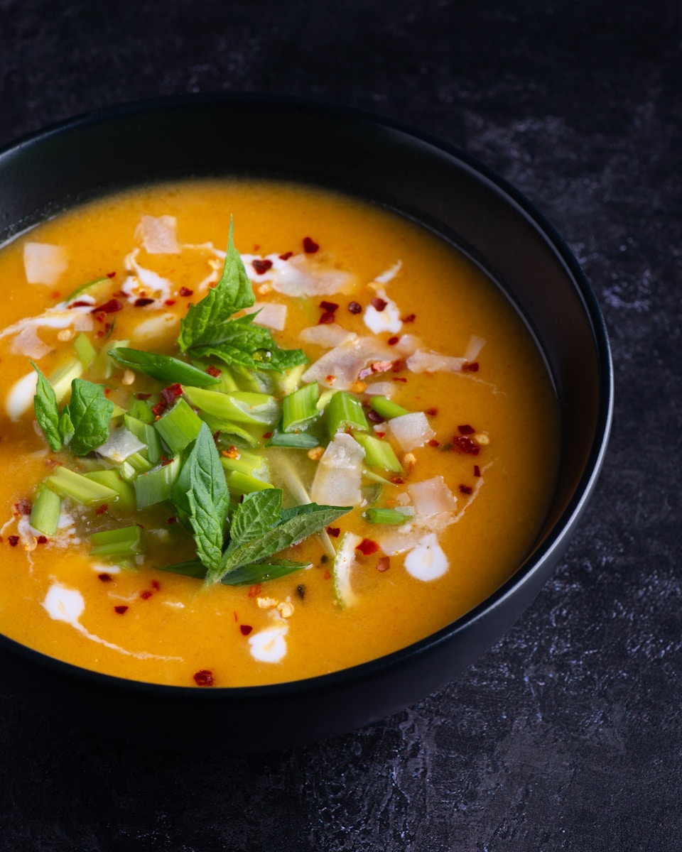 thai pumpkin soup soup with green leaf on black ceramic bowl