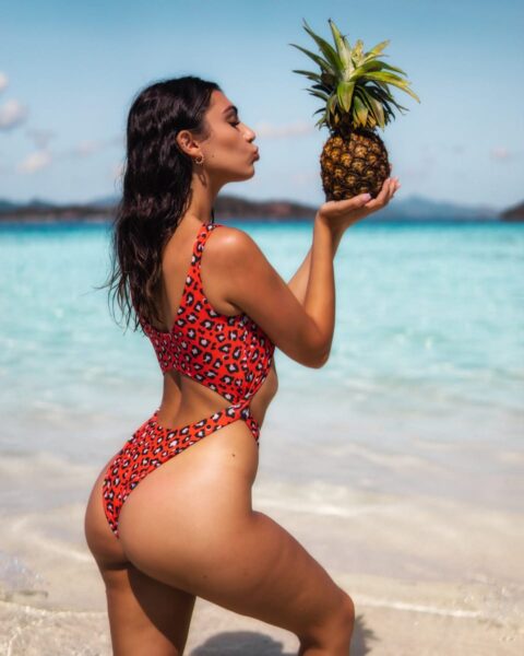 Brazilian Butt Lift, woman in red and white polka dot bikini holding pineapple on beach during daytime
