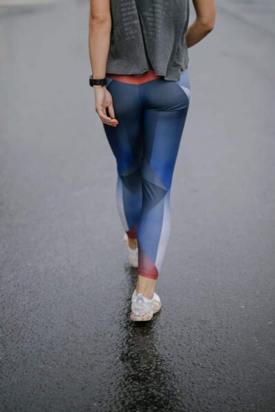 A woman in colorful leggings walks on a wet pavement, showcasing casual activewear style.