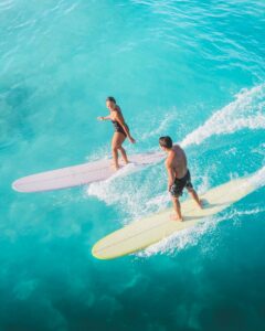 Dynamic aerial photo of male and female surfers gliding on turquoise ocean waves.