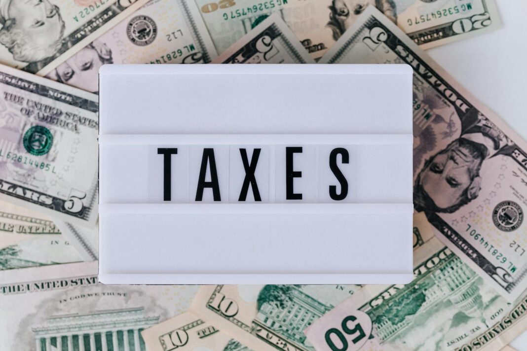 IRS Stimulus - Top view of white vintage light box with TAXES inscription placed on stack of USA dollar bills on white surface