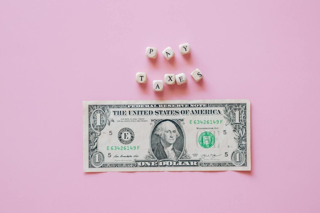 US one dollar bill on a pink background with pay taxes reminder cubes.