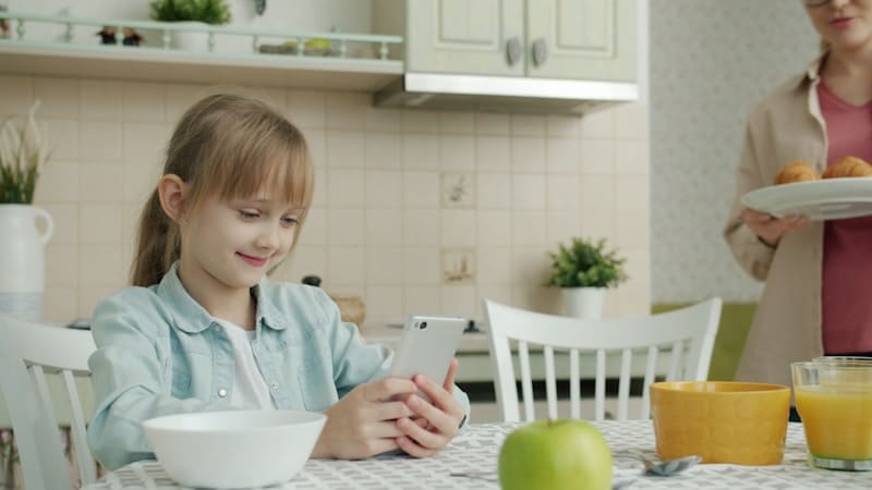 Smartphone - Girl using phone at kitchen table with breakfast