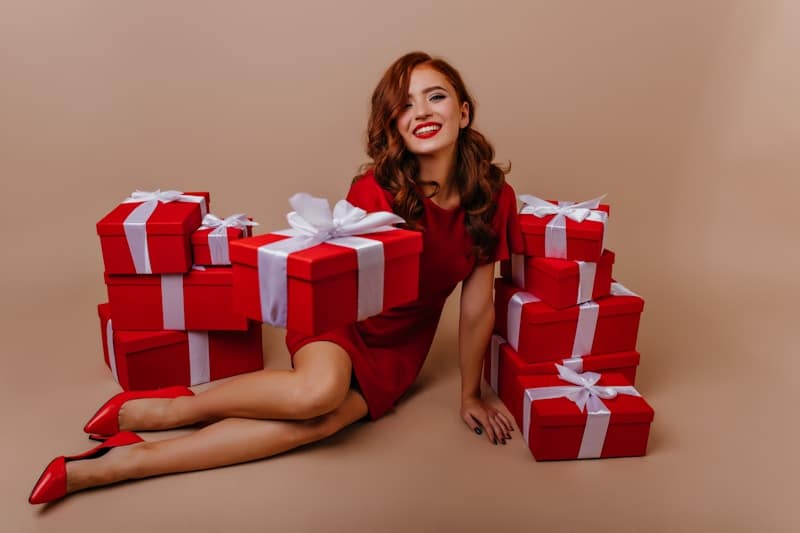 Christmas Gifts for Women - a woman in a red dress sitting on the floor with many wrapped presents