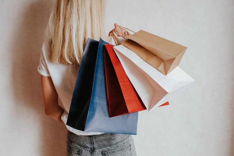 Woman holding colorful shopping bags against a wall.