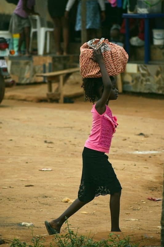 A young girl carrying a basket on her head
