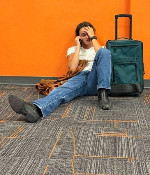 Stuck travelers Man sitting on floor with suitcase, looking distressed.